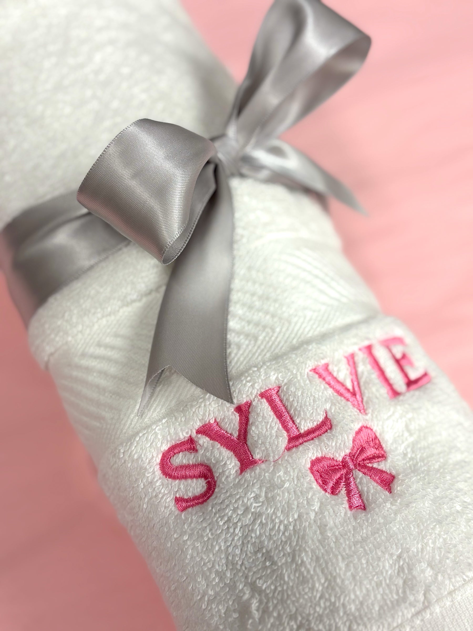 Close up of a personalized baby towel with the name Sylvie and a pink bow embroidered in pink thread