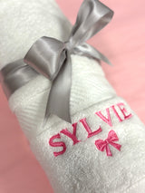 Close up of a personalized baby towel with the name Sylvie and a pink bow embroidered in pink thread