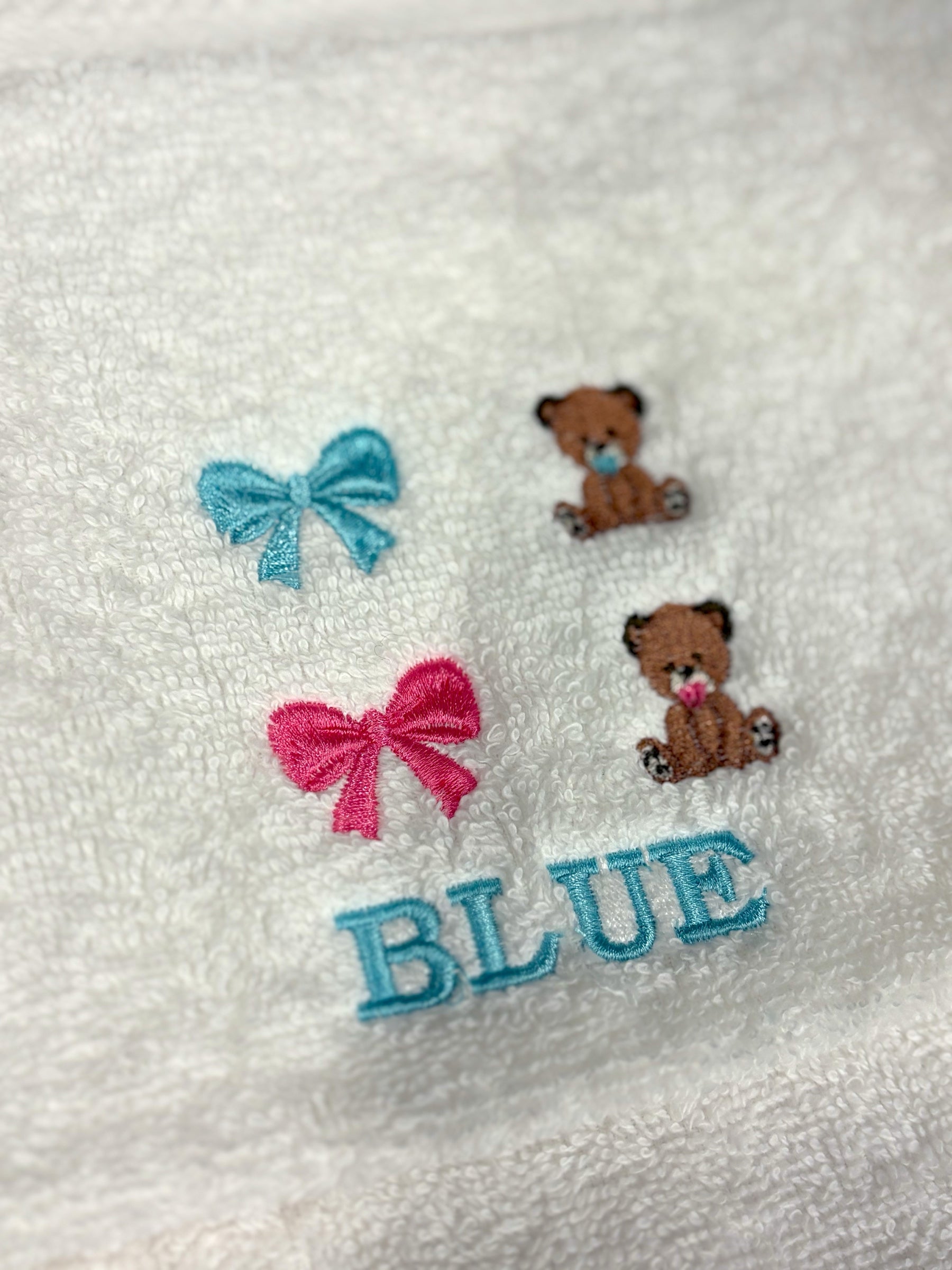 Embroidery design options on a white towel: blue bow, pink bow, blue bear and pink bear, with a name sample in blue thread